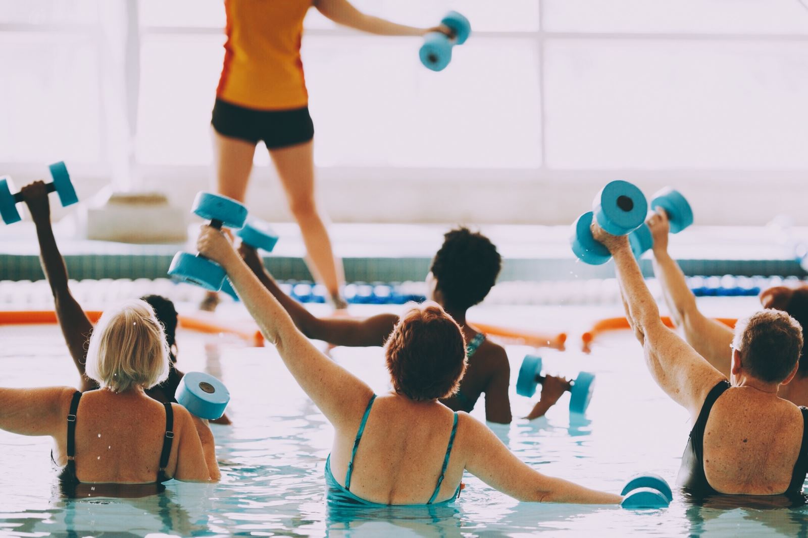 Group of people in pool doing aqua fit exercises with dumbbells, led by instructor